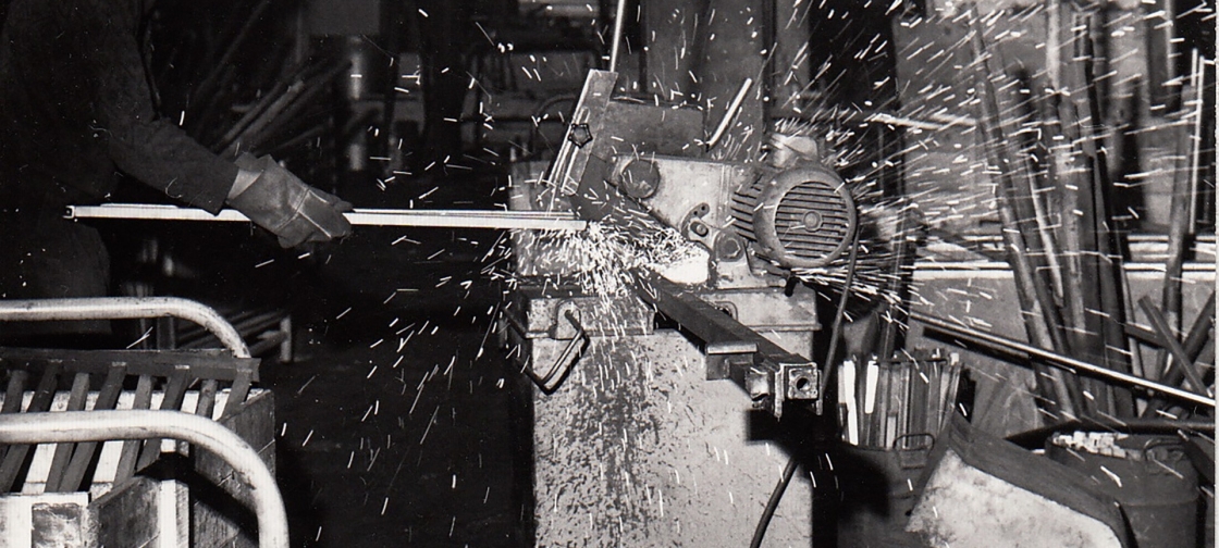 Photo en noir et blanc d’un ouvrier usinant un rayonnage dans les années 1970
	                        