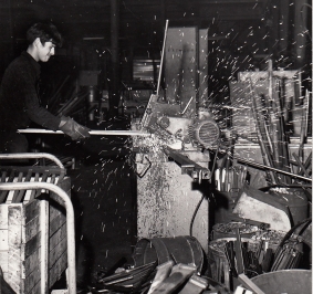 Photo en noir et blanc d’un ouvrier usinant un rayonnage dans les années 1970
			