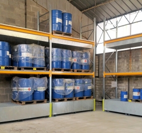 Rayonnages lourds avec des bacs de rétention utilisés pour stocker des fûts de produits chimiques dans un hangar
			